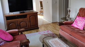 Ett vardagsrum med en platt-TV, ett träskåp, en röd soffa och ett soffbord i glas.