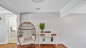 Um quarto com uma cadeira suspensa, um console branco com plantas e piso de madeira.