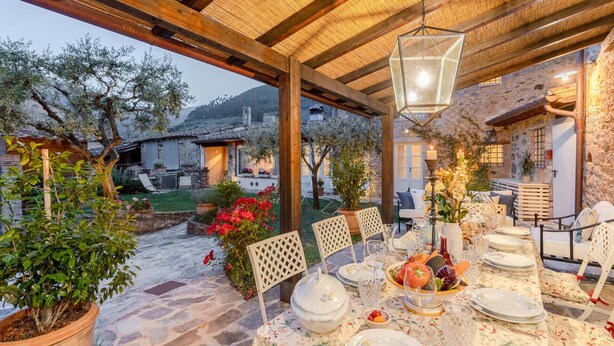 An outdoor dining area with a stone floor, wooden pergola, and a table set for a meal. - Dimora delle Camelie, a traditional stylish stone farmhouse with garden on the hills of Compitese between Lucca and Pisa (Pieve di Compito)