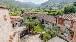 A courtyard with stone buildings, a small garden, and a mountainous backdrop. - Dimora delle Camelie, a traditional stylish stone farmhouse with garden on the hills of Compitese between Lucca and Pisa (Pieve di Compito)