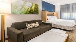 A hotel room with a sofa, a bed, a wall-mounted artwork, and a lamp.