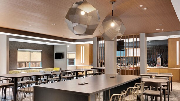 A modern hotel lobby with a central bar area, multiple seating arrangements, and large windows providing views of the outside.