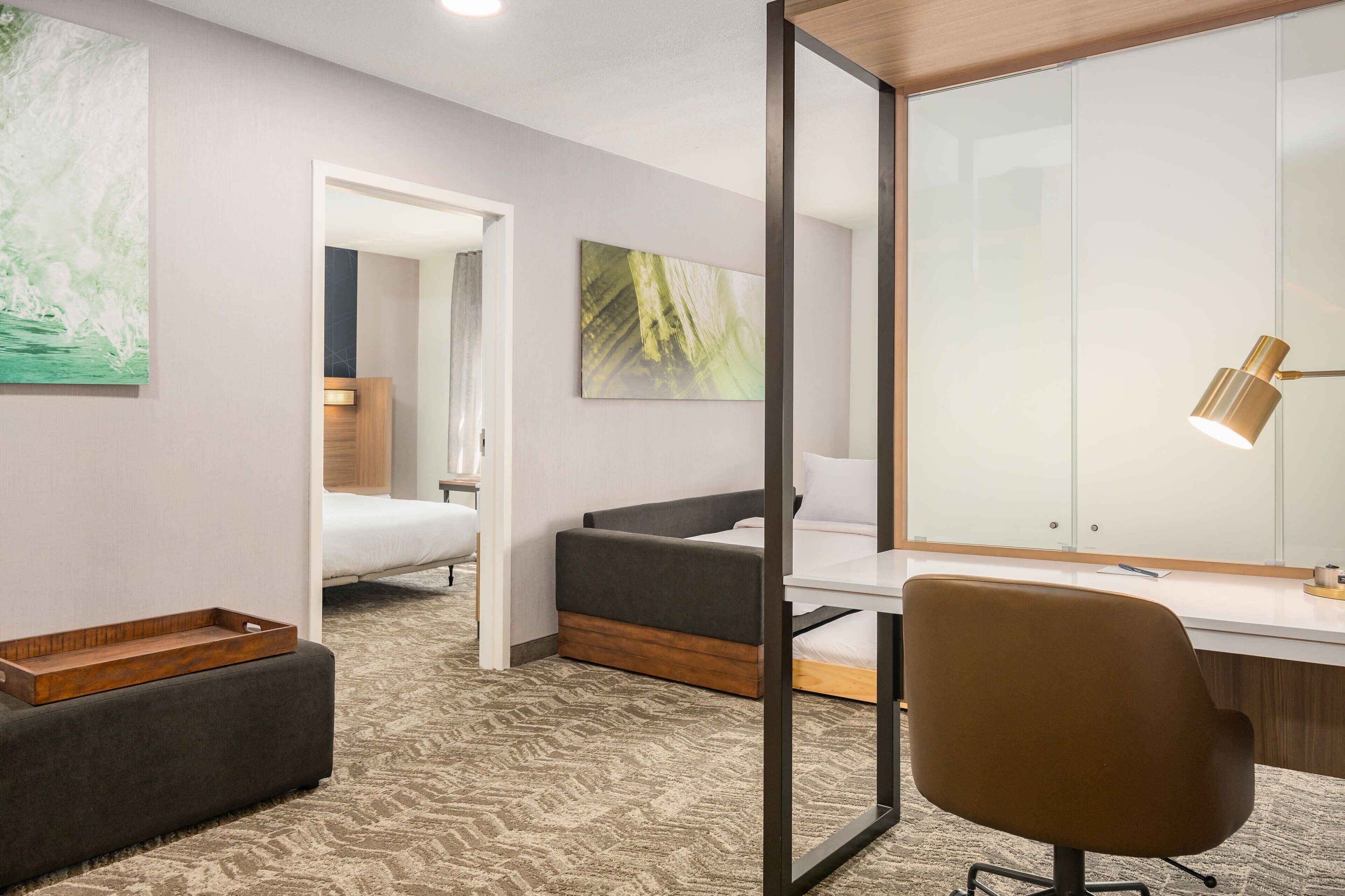 A modern hotel room with a bed, a desk, a chair, and a large mirror.