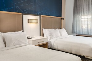 Una habitación de hotel con dos camas, una mesita de noche con teléfono e iluminación empotrada en la pared.