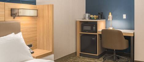 A hotel room with a bed, a desk with a computer, a microwave, a coffee maker, and a lamp.
