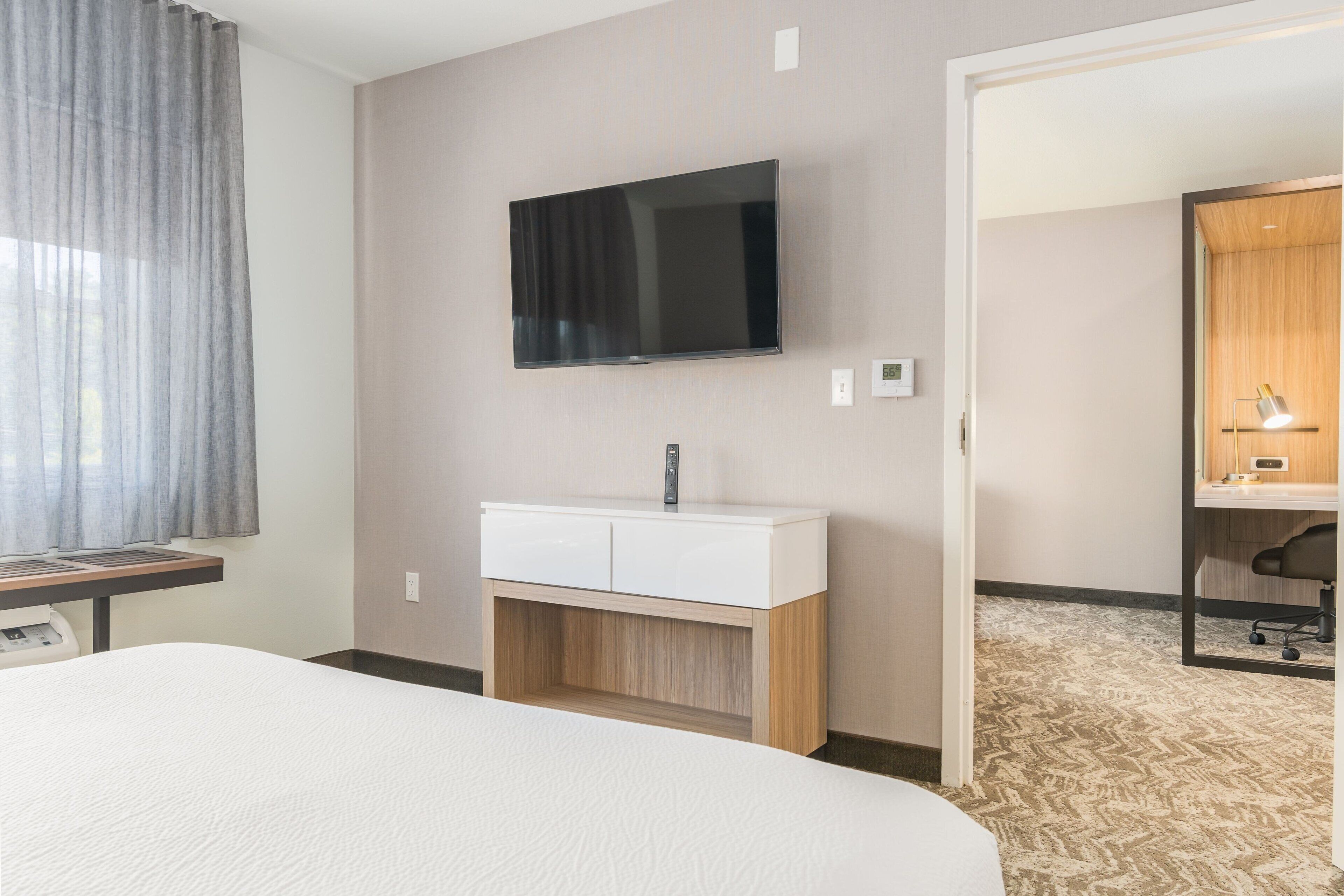 Een hotelkamer met een bed, een aan de muur bevestigde televisie, een houten kast en een bureau met stoel.