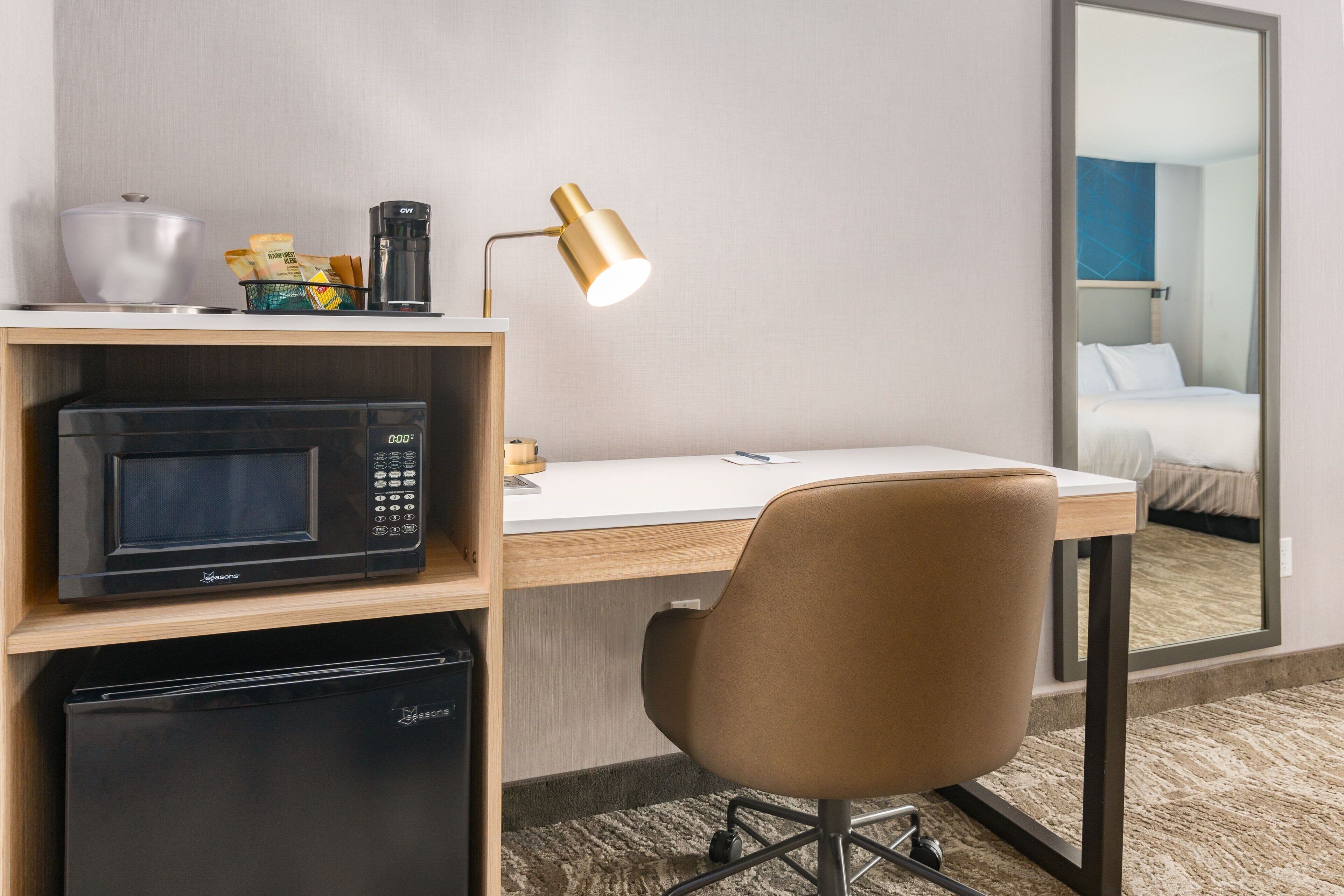Habitación de hotel con microondas, cafetera y escritorio con silla.