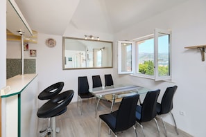 A modern dining area with a glass table and black chairs, a large mirror, and a view of greenery through a window. - Joyful Place - Three Bedroom Apartment, Sleeps 6 (Dubrovnik)