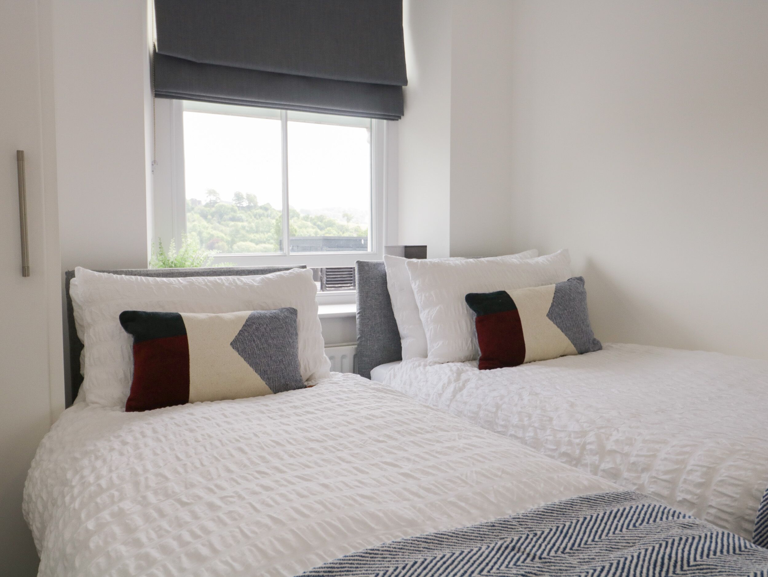 A hotel room with two beds, white bedding, and a window with a view of greenery.
