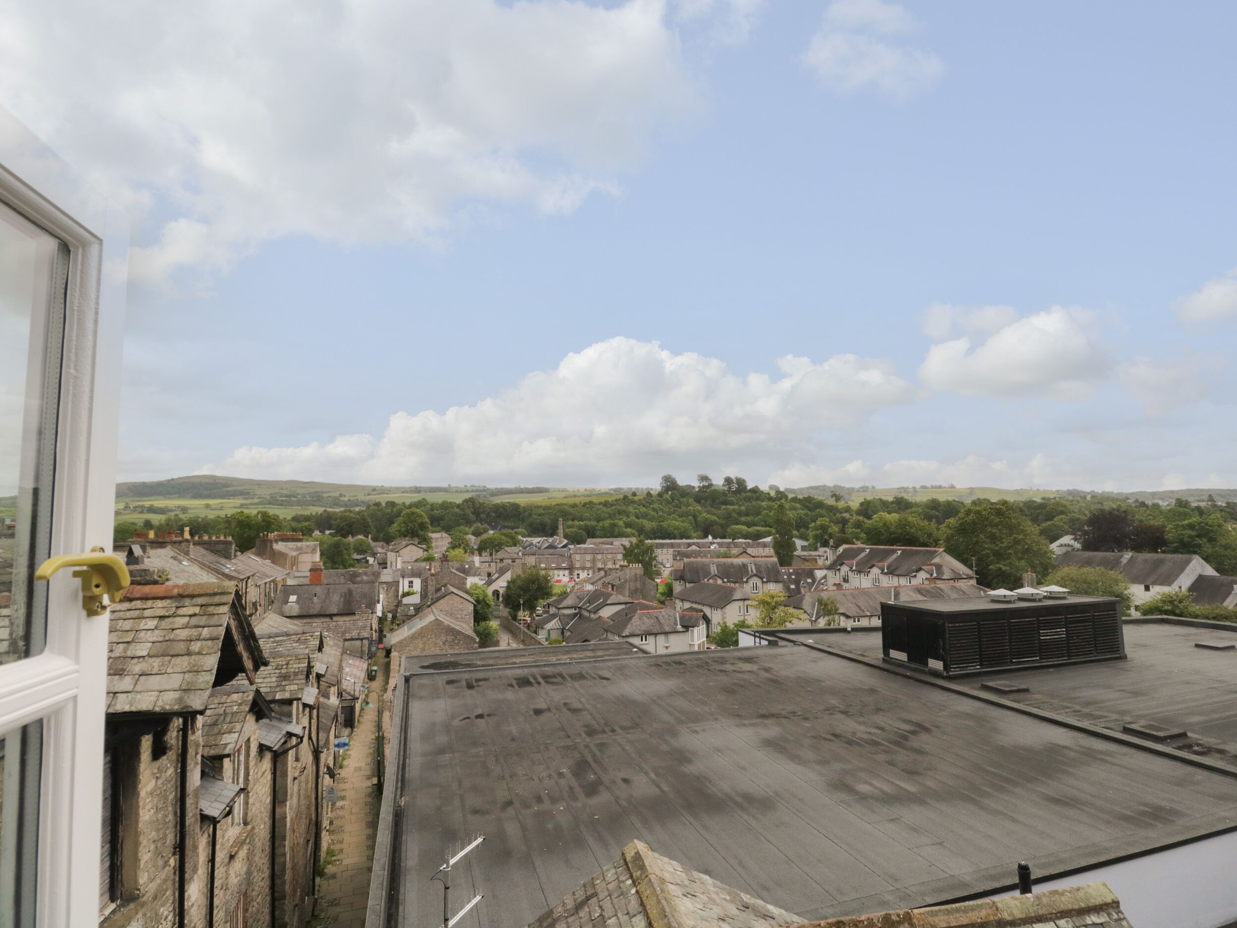 Une vue sur une ville, prise depuis une fenêtre donnant sur une rue bordée de bâtiments traditionnels et d’une construction à toit plat.