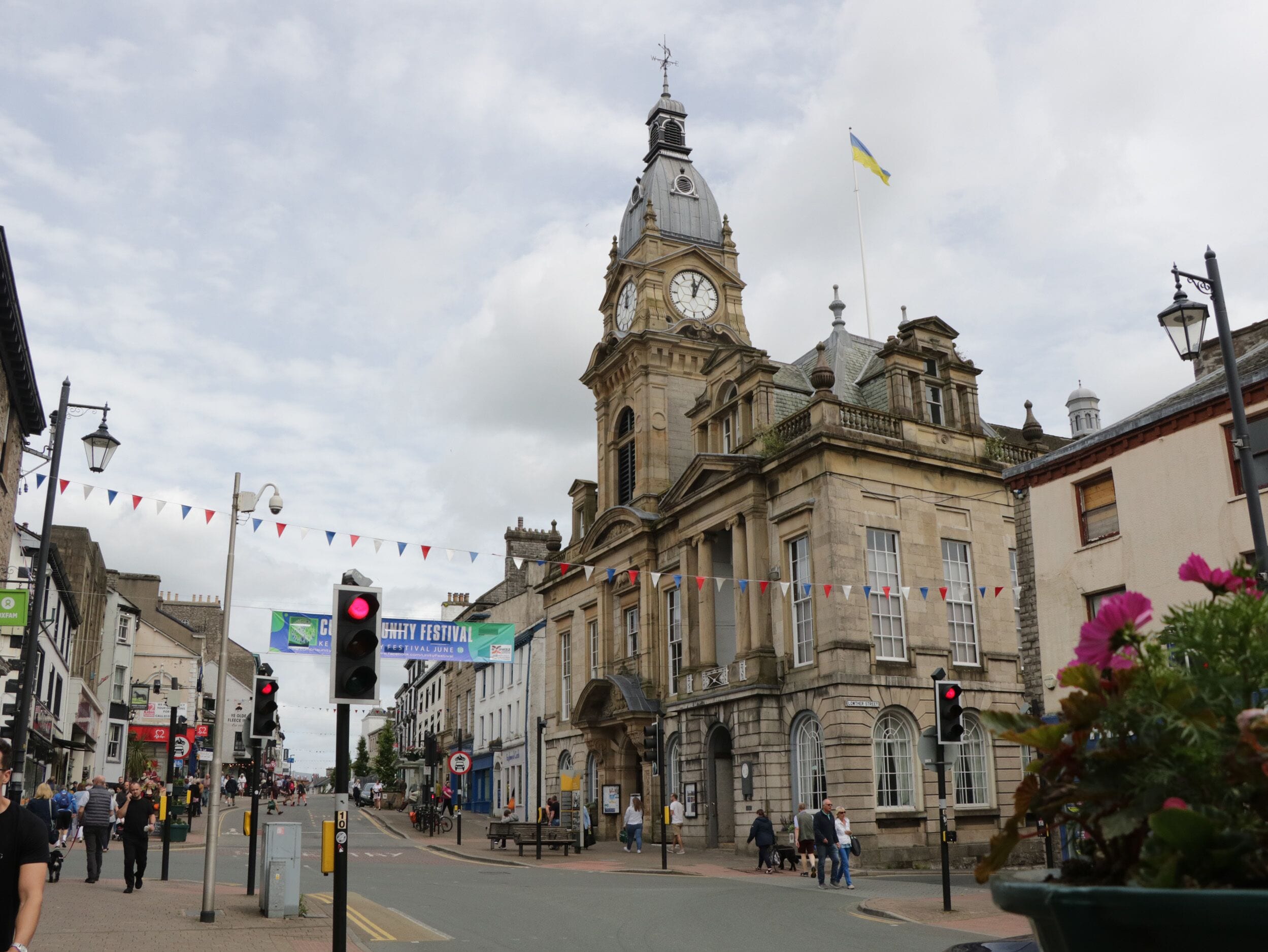 A historic building with a clock tower, a street with pedestrians, and a blue banner indicating a festival.
