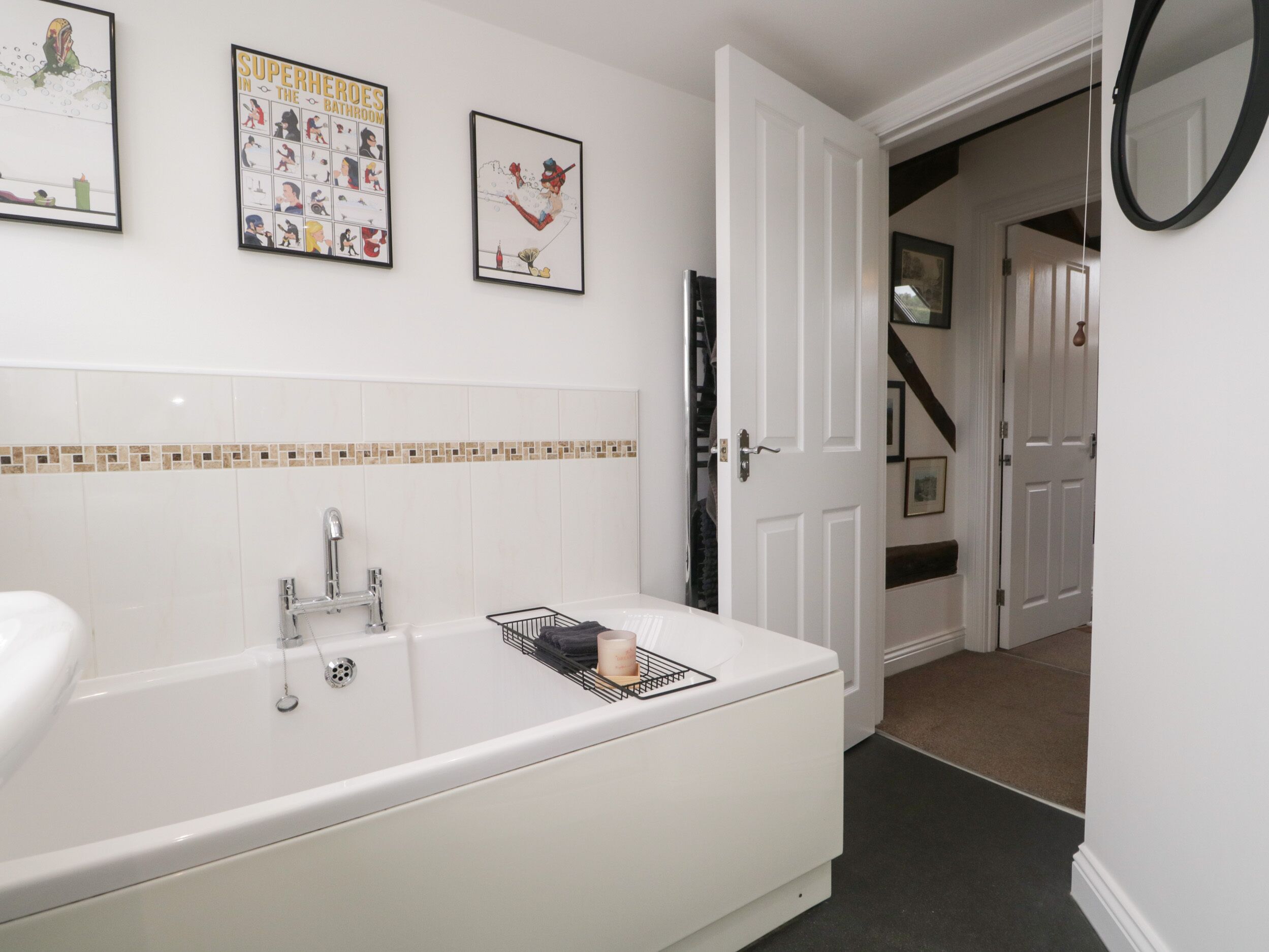 A bathroom with a white bathtub, a sink, and a tiled backsplash. There are framed pictures on the wall and a door leading to another room.