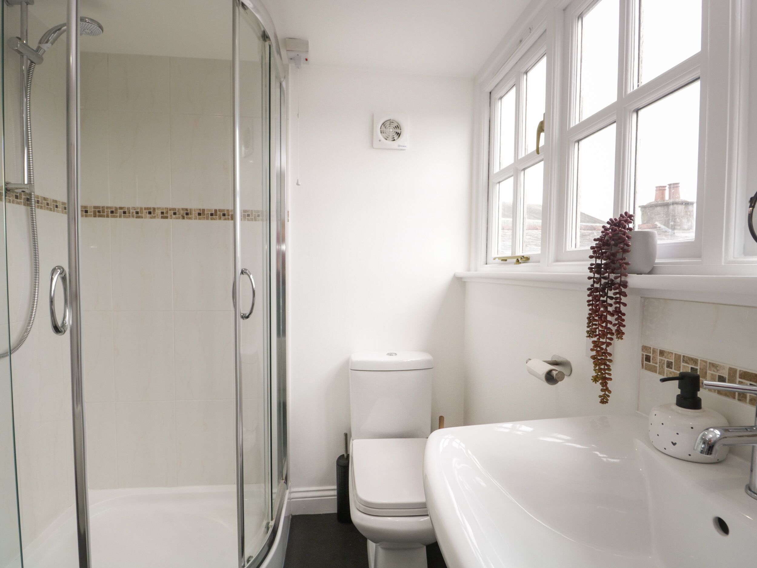 A bathroom with a glass-enclosed shower, a white toilet, and a sink with a soap dispenser.