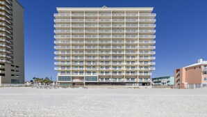 A multi-story hotel with a uniform exterior, located on a beach with a clear sky. - Crystal Shores 606 | Unforgettable Gulf Front Views | Indoor & Outdoor Pools (Gulf Shores)