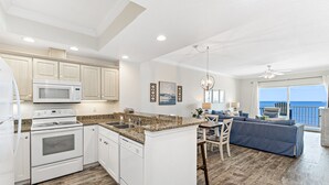 A modern kitchen with white cabinetry, a built-in microwave, and a granite countertop. - Crystal Shores 606 | Unforgettable Gulf Front Views | Indoor & Outdoor Pools (Gulf Shores)
