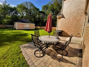 A patio with a round table and chairs, a red umbrella, and a brick wall.