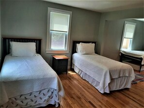 A room with two beds, wooden flooring, and a window.