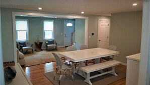 A spacious living room with a large white dining table, several chairs, a bench, and a sofa. There are two windows with blinds, a door, and a staircase leading to another room. - Beautiful home!!! Private game room, swimming pool and pets allowed. (Sandwich)