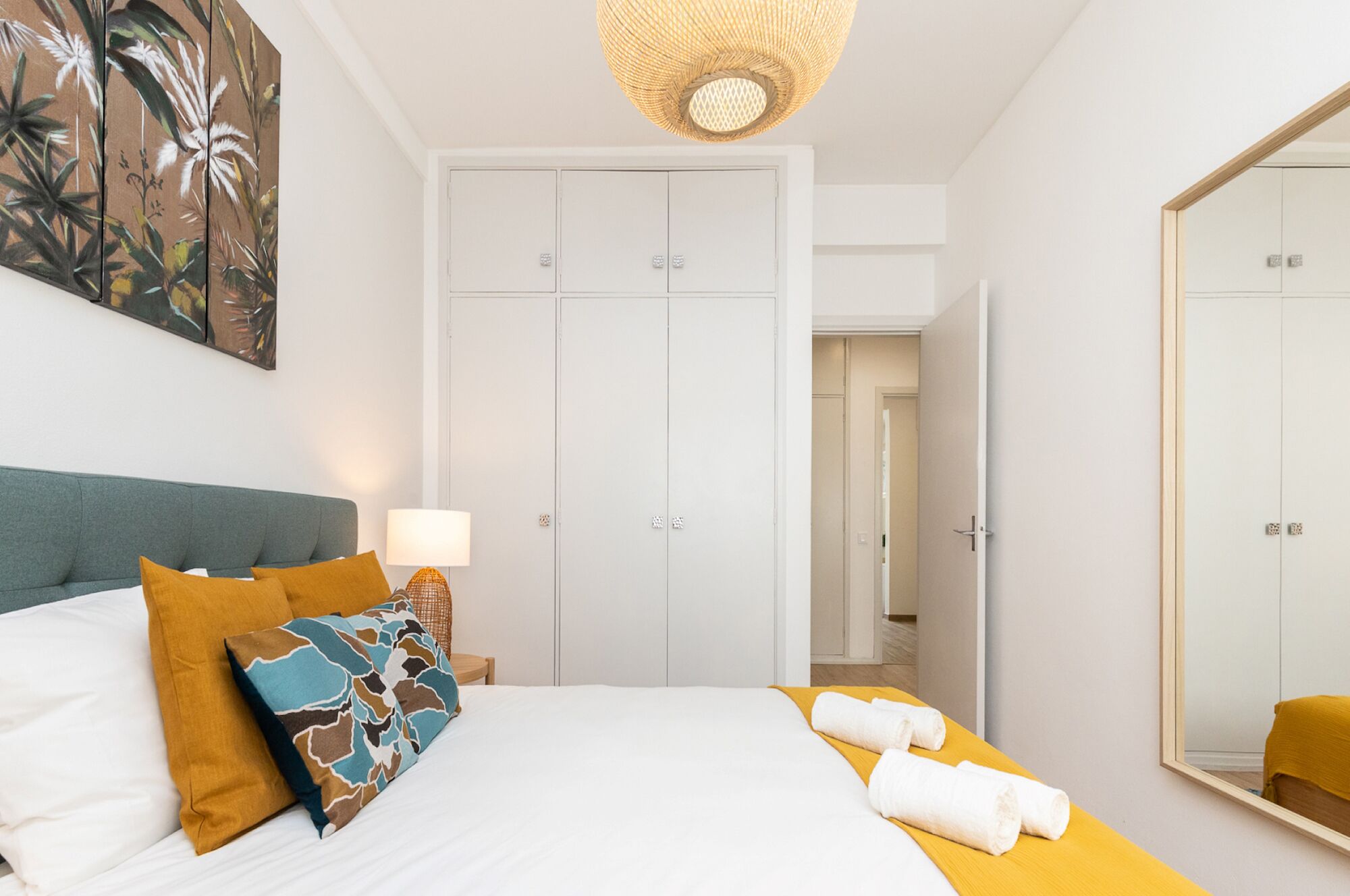 A hotel room with a bed, a nightstand, a lamp, a mirror, and a wardrobe.