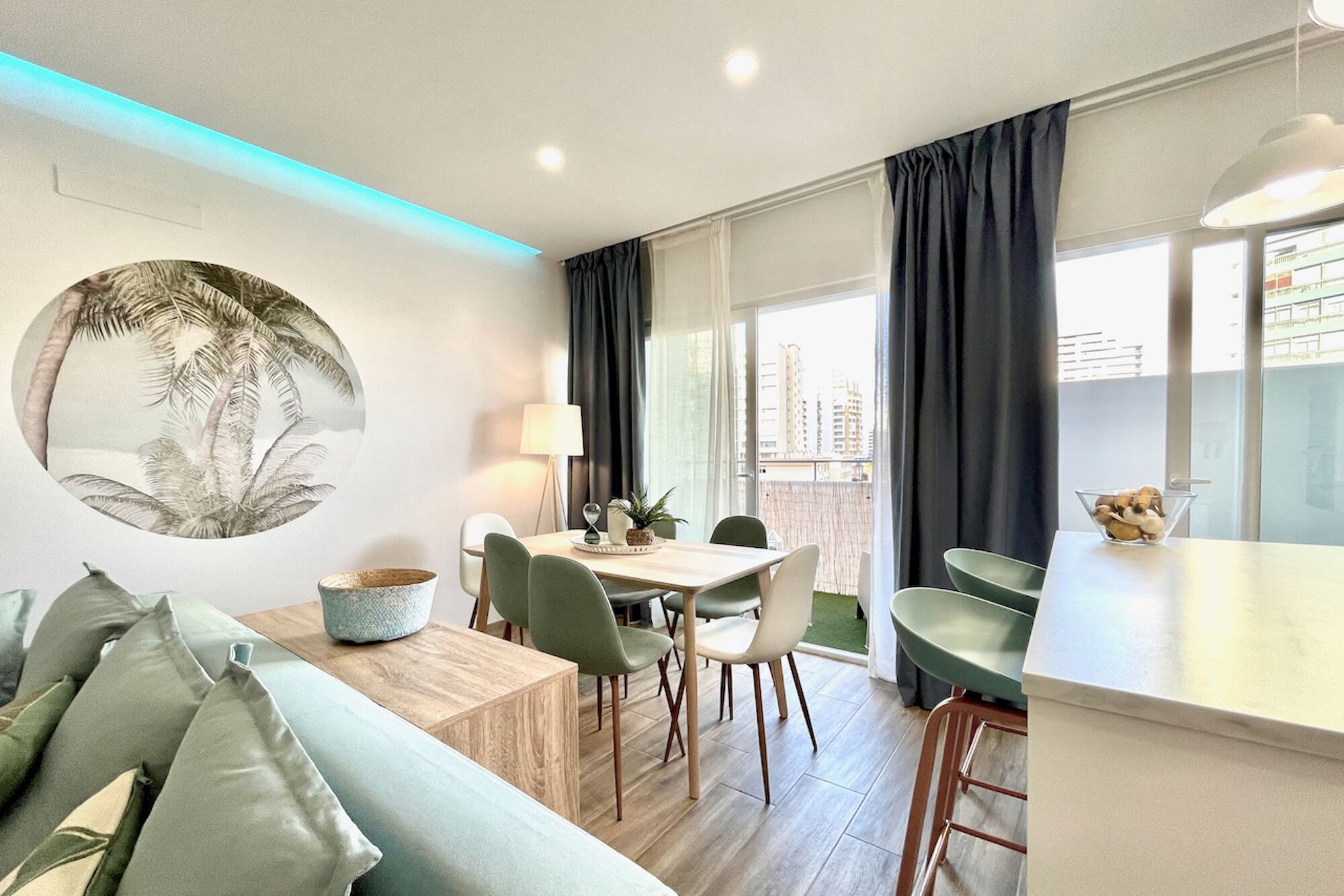 Un salón moderno con una mesa de centro de madera, sillas verdes y un gran cuadro circular en la pared.