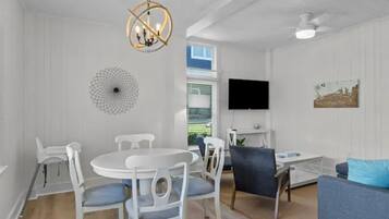 A room with a dining table and chairs, a sofa, a TV, and a chandelier.