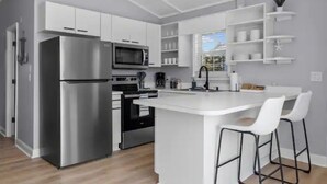 Una cocina moderna con gabinetes blancos, electrodomésticos de acero inoxidable y una isla central con taburetes de bar.