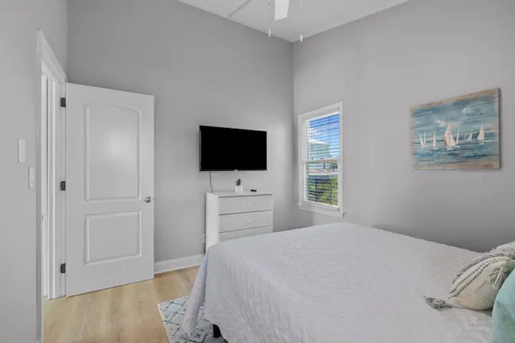 A bedroom with a bed, a dresser, a television, and a window with blinds.