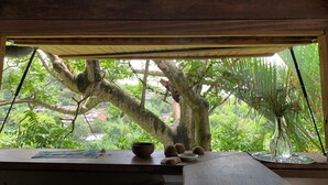 A wooden ceiling with a woven light fixture, a wooden table with a bowl, pottery, and a vase, and a view of a tree and greenery outside. - ecolodge Martinique (Fort-de-France)