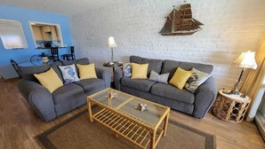 A living room with two grey sofas, a glass coffee table, and a ship decoration on the wall. - King 1bd/1ba Condo w/ Pool View & Beach Access (Port Aransas)