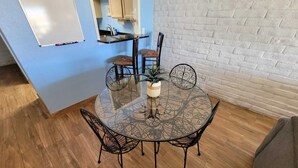A round glass table with metal chairs, a potted plant, and a whiteboard on a blue wall. - King 1bd/1ba Condo w/ Pool View & Beach Access (Port Aransas)