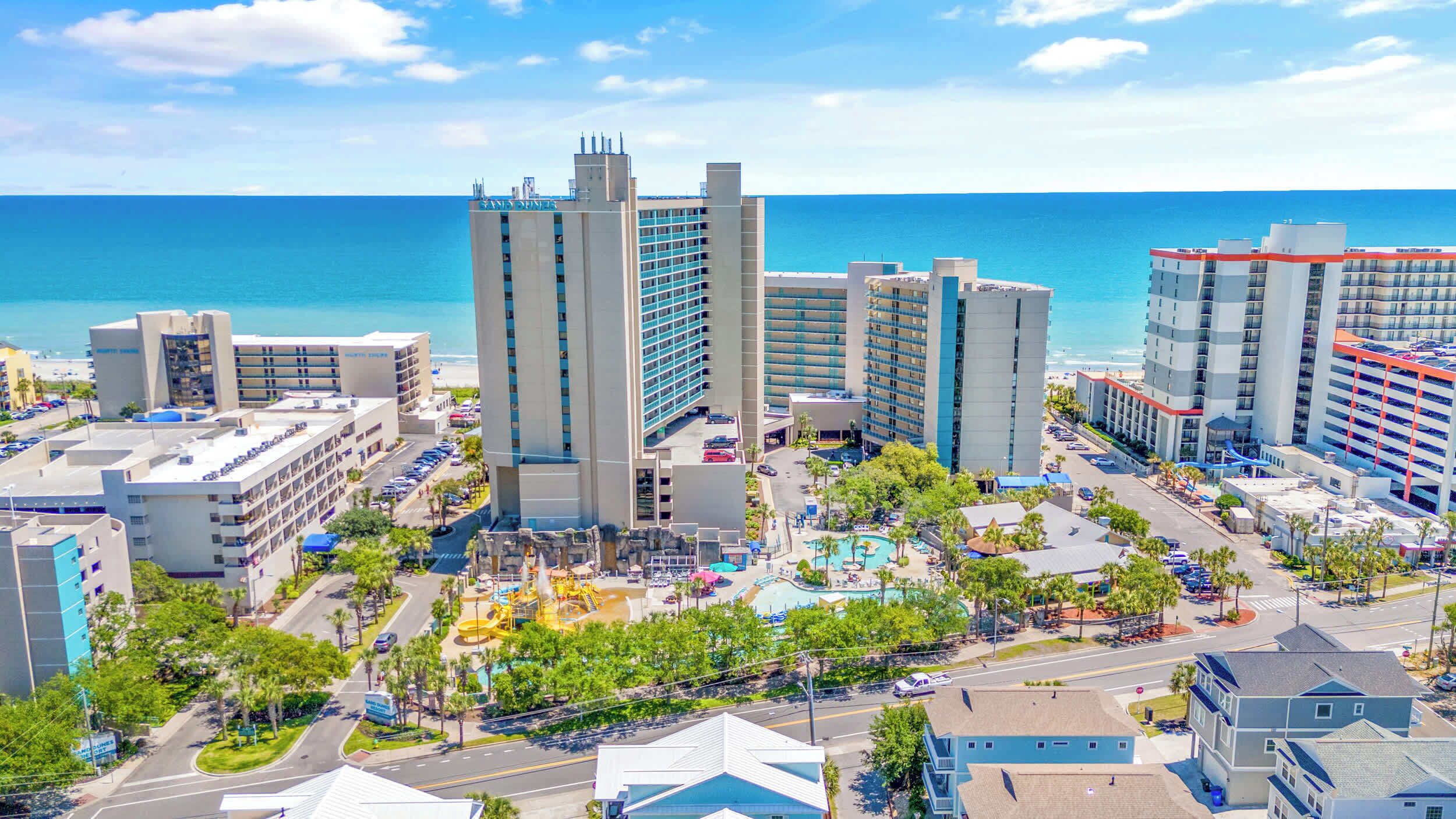 A coastal hotel complex with multiple high-rise buildings, a swimming pool, and a beach view.