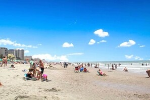 A beach with people sunbathing and swimming, and buildings in the background.