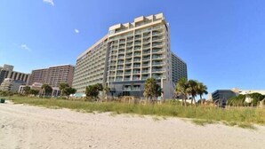 A multi-story hotel with a flat roof, located near a sandy beach. - Paradise Ocean View at Sand Dunes Resort (Myrtle Beach)