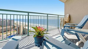 A balcony with a view of the beach, a potted plant, and blue lounge chairs. - Paradise Ocean View at Sand Dunes Resort (Myrtle Beach)