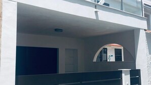 Un edificio moderno de dos pisos con balcón, cochera y un ventanal pequeño.