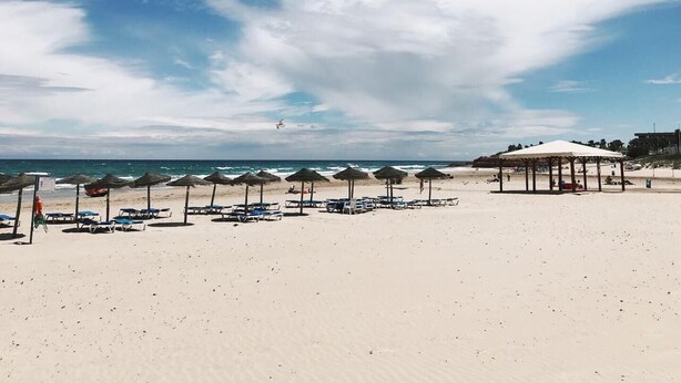 Una playa con sombrillas, sillas de descanso y un pabellón.