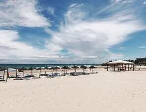 Ein Strand mit Sonnenschirmen, Liegestühlen und einer Strandpergola.