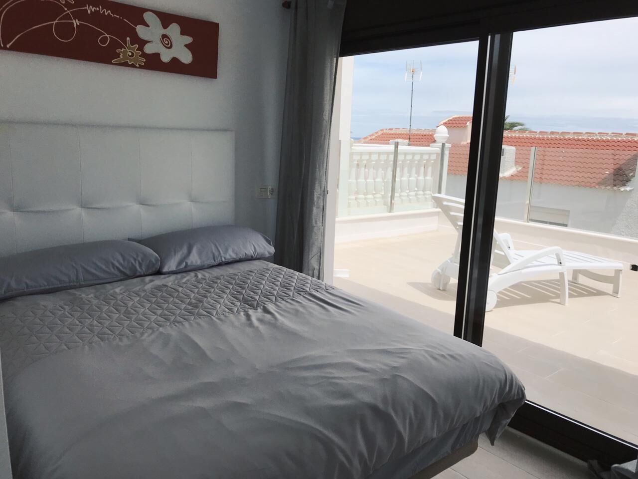 Ein Schlafzimmer mit einem großen Bett, Blick auf die Terrasse und einem dekorativen Wandbild.