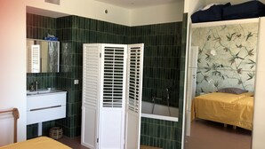 A room with a bed, a bathroom with a shower, and a small sitting area. - RIOPASSIONS, LARGE T3, BEAUTIFUL SEA VIEW (Toulon)