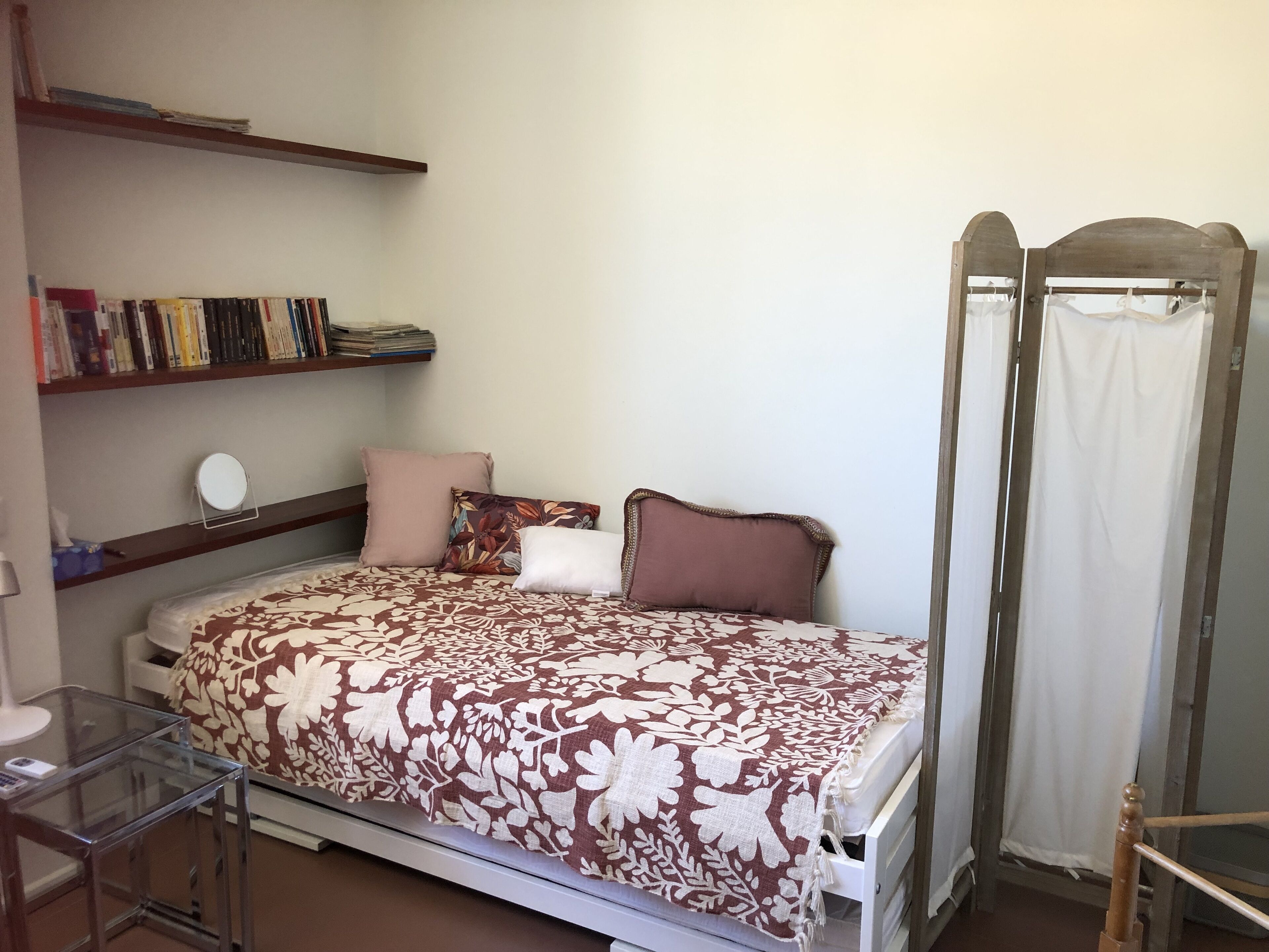 Ein Schlafzimmer mit Bett, Nachttisch, Spiegel, einer Bücherablage und einem Kleiderschrank.