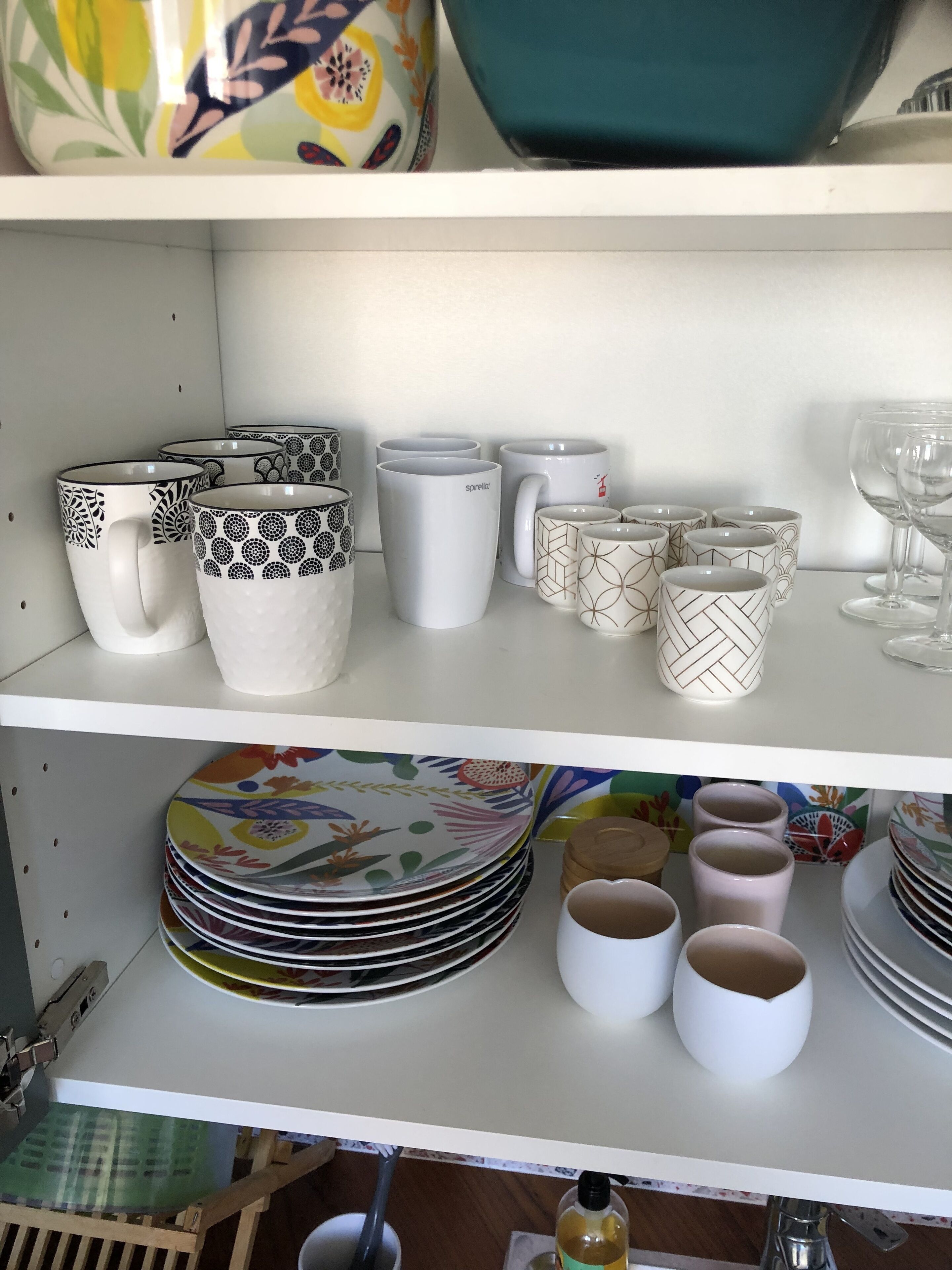 A shelf with various kitchenware including mugs, plates, and bowls.