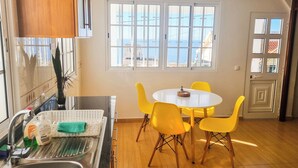 Une cuisine équipée d’un évier, une table à manger avec des chaises jaunes et une fenêtre donnant sur la mer.