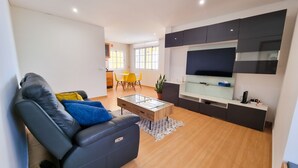 Un salon moderne avec un canapé noir, une table basse en verre et un téléviseur à écran plat fixé au mur.
