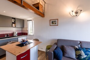A compact kitchen with a wooden island, a dining area, and a grey sofa with decorative pillows. - Ambroggio - Grand studio avec mezzanine - Vue Mer (Lumio)