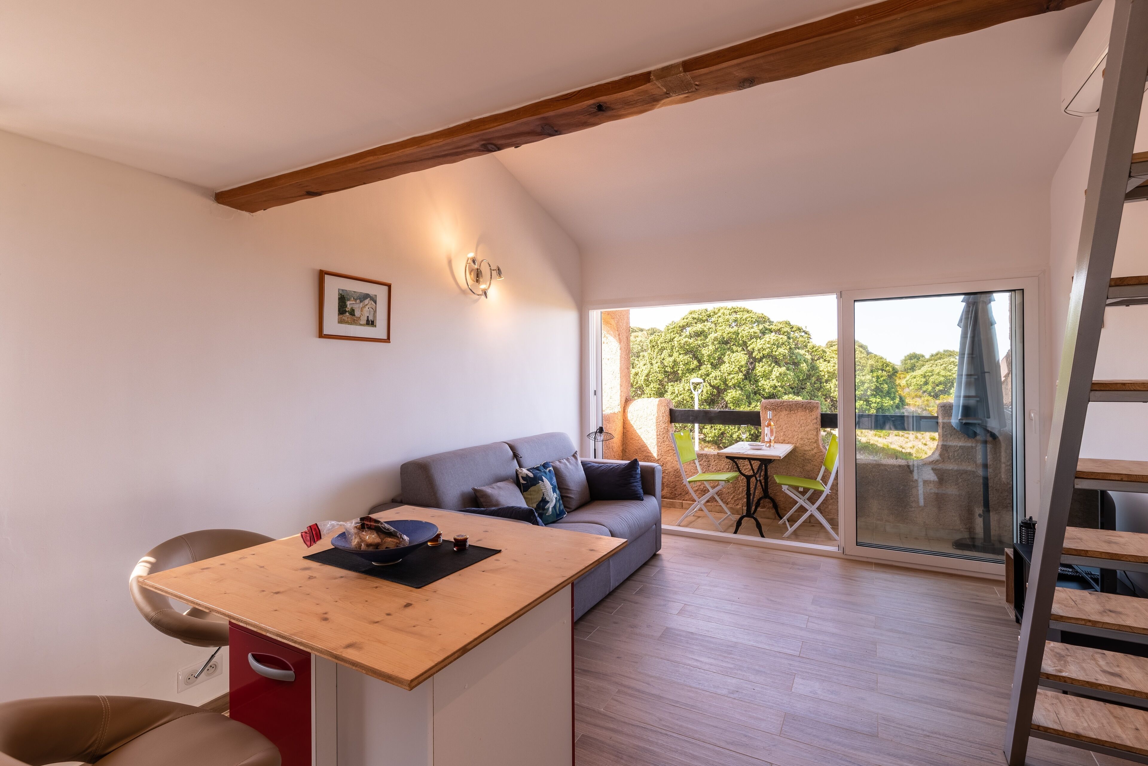 Un espace de vie moderne comprenant une table à manger en bois, un canapé et un balcon offrant une vue sur la verdure.