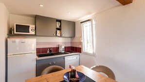 A compact kitchen with a microwave, coffee maker, and a small refrigerator. There is a dining table with chairs and a window providing natural light. - Ambroggio - Grand studio avec mezzanine - Vue Mer (Lumio)