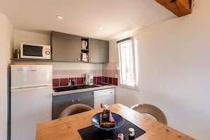 Cozinha compacta com micro-ondas, cafeteira e pequena geladeira. Há uma mesa de jantar com cadeiras e uma janela que oferece iluminação natural.