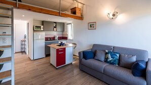 A modern apartment with a loft bedroom, a kitchenette, and a living area with a sofa and cushions. - Ambroggio - Grand studio avec mezzanine - Vue Mer (Lumio)