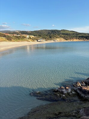 Eine Küstenlandschaft mit klarem Wasser, einem Sandstrand und einigen Gebäuden im Hintergrund.