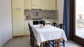A compact kitchen with yellow cabinets, a dining table set for two, and a view of the outside through a window. - Libeccio | Relax Terrace 30m from the beach (Isola Rossa)